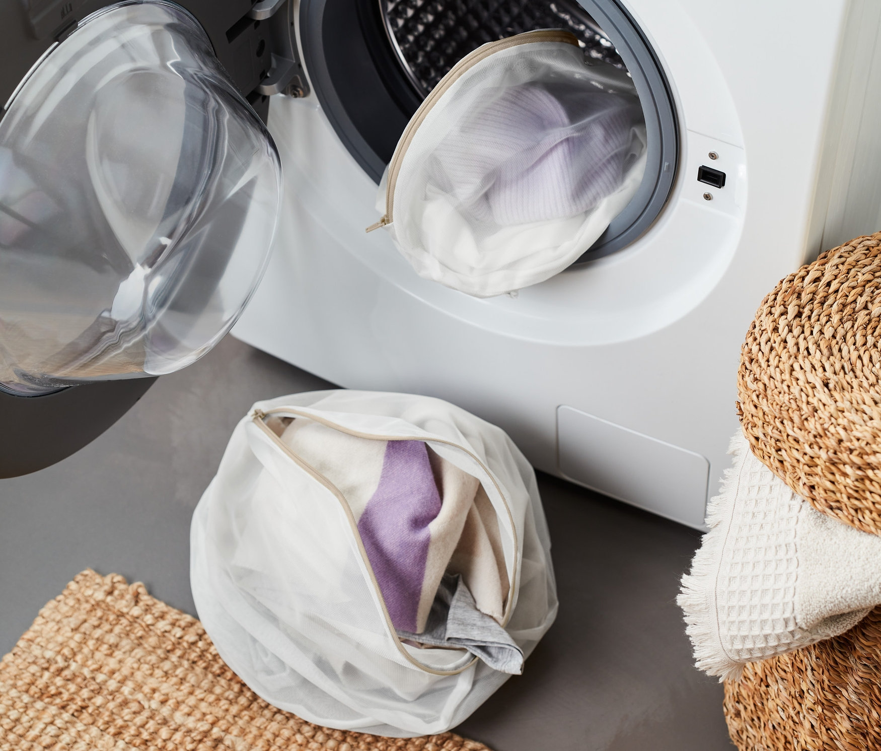 İki adet çamaşır yıkama filesi, biri çamaşır makinesinde, diğeri paspasın yanında yerde.