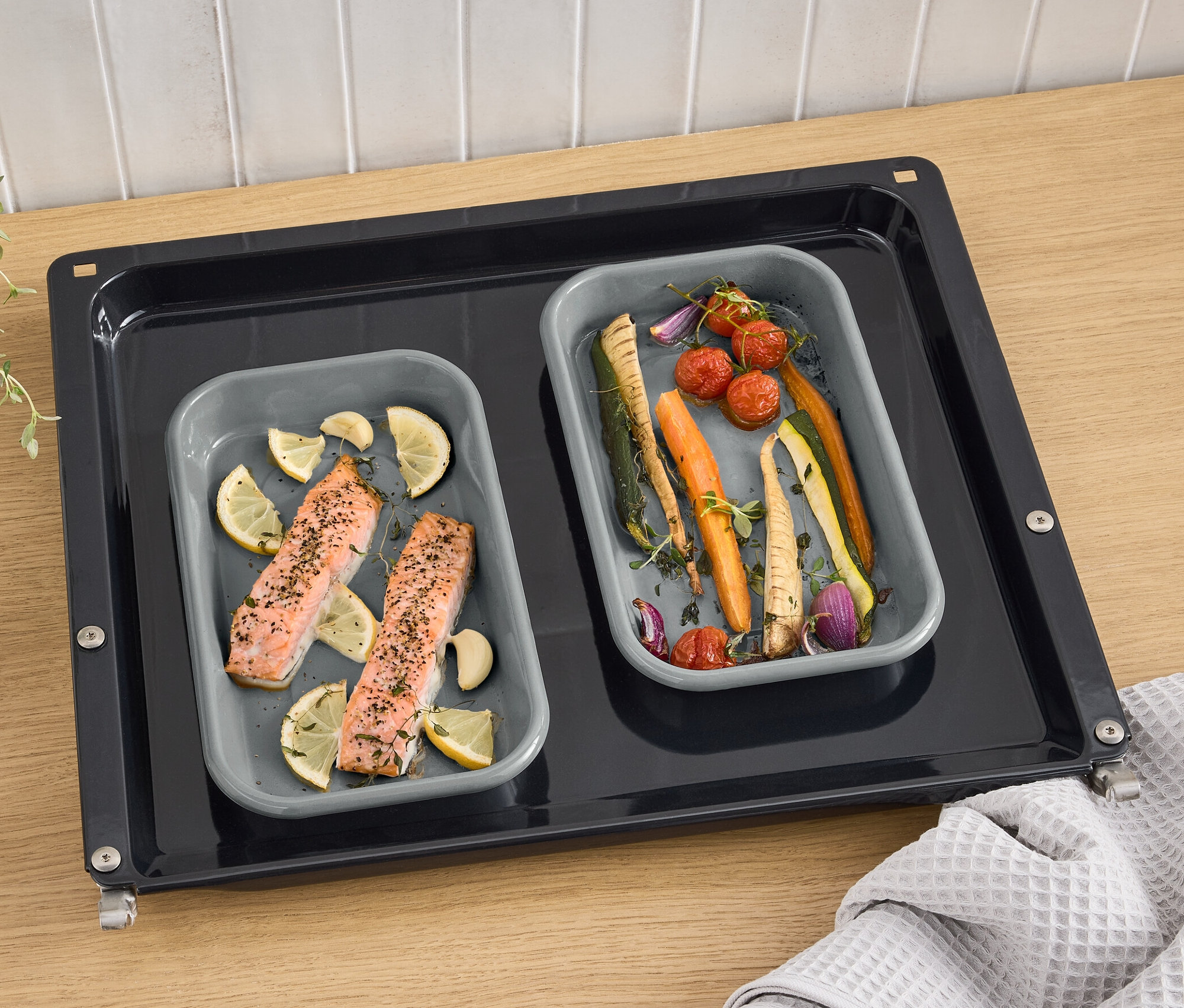 Fırın tepsisinde somon, limon ve sebzelerle birlikte iki adet gri emaye ızgara kabı.