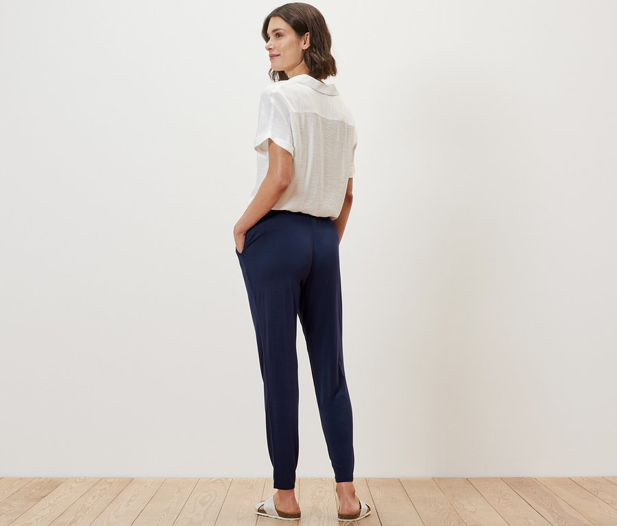 Kadın kameraya arkası dönük duruyor ve lacivert jarse pantolon giyiyor.