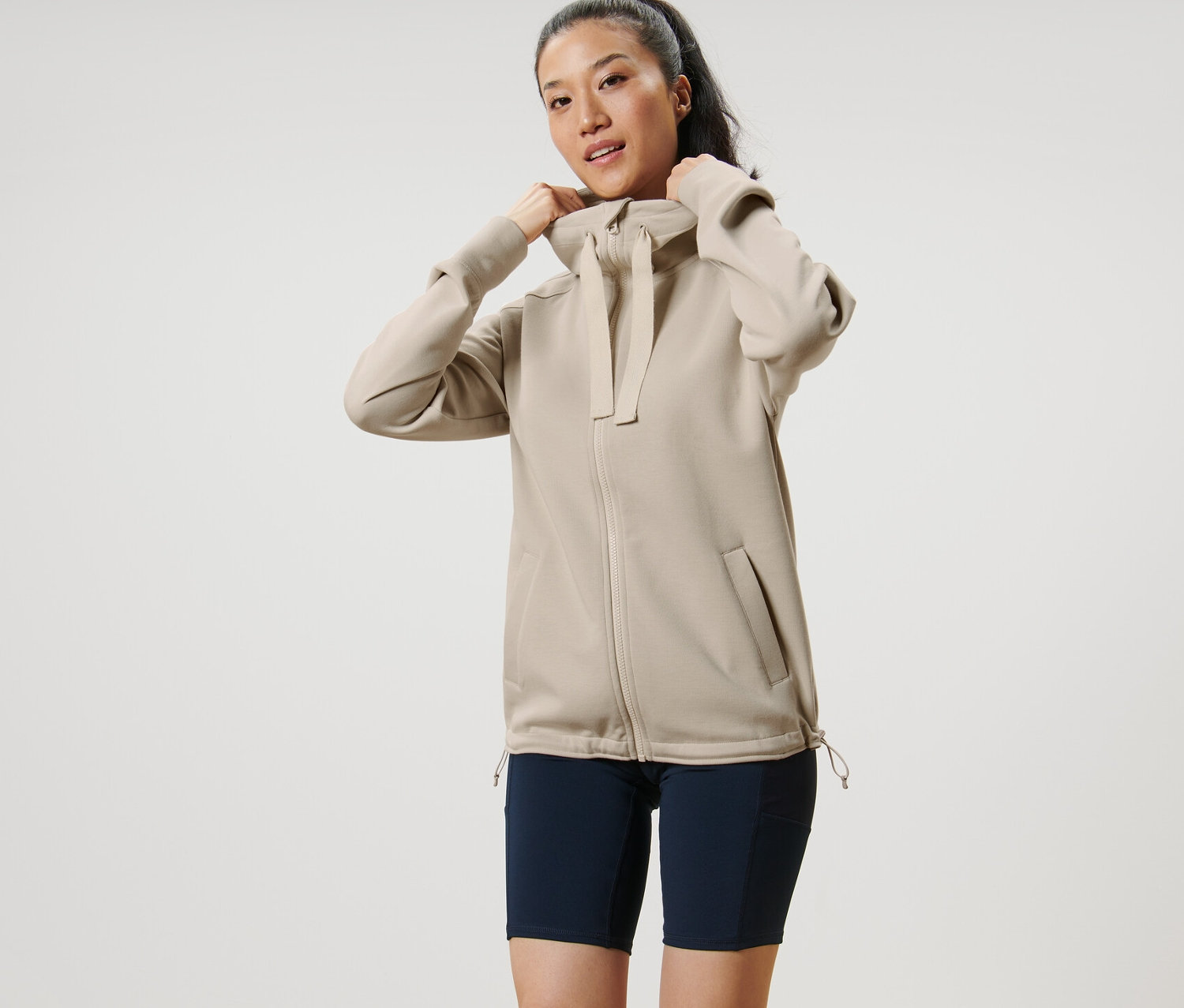 Kadın bej kapüşonlu sweat ceketinin kapüşonunu ayarlıyor.