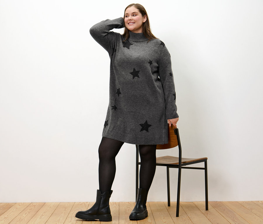 Kadın balıkçı yaka örgü elbise, siyah çizme ve külotlu çorapla poz veriyor.