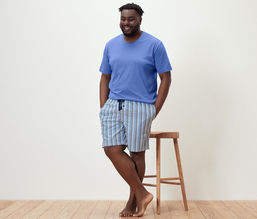 Adam tabureye yaslanmış, şortlu pijama takımı giyiyor.