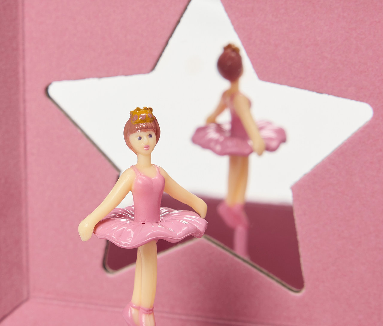 Taçlı pembe bir balerin figürü, yıldız şeklinde bir aynanın önünde duruyor.