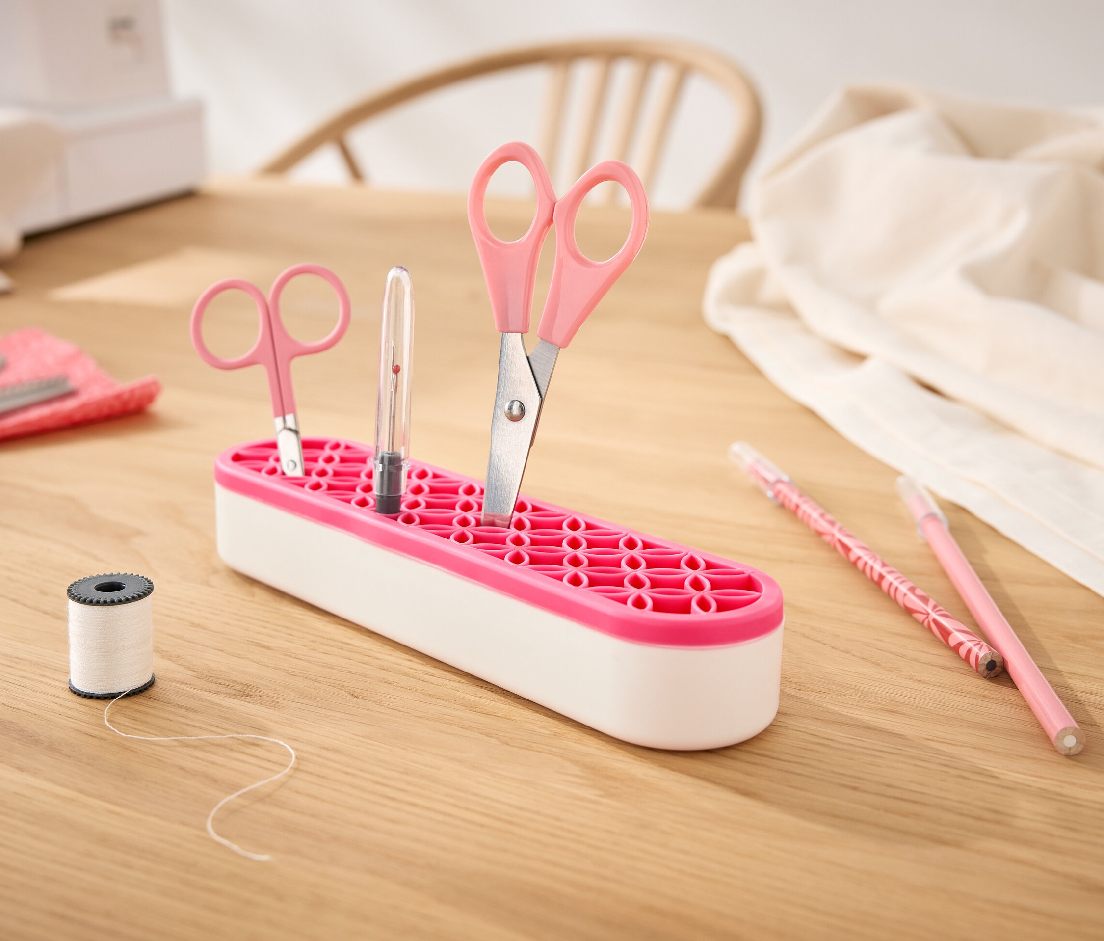 Ahşap bir masa üzerinde çok amaçlı bir düzenleyicide makas ve kalem bulunmaktadır.