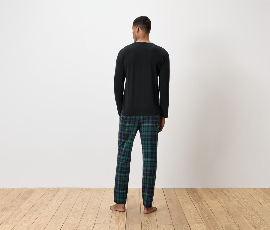Arkası dönük bir adam, uzun kollu siyah bir tişört ve yeşil ekose bir pijama altı giyiyor.