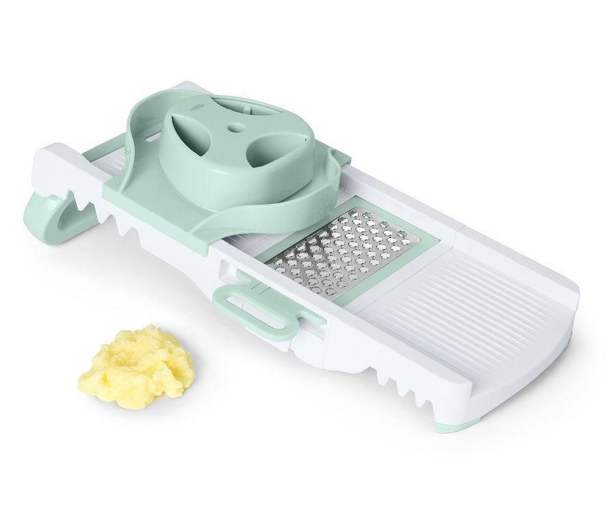 Doğranmış sebze yığını olan beyaz ve yeşil renkli mandolin dilimleyici.