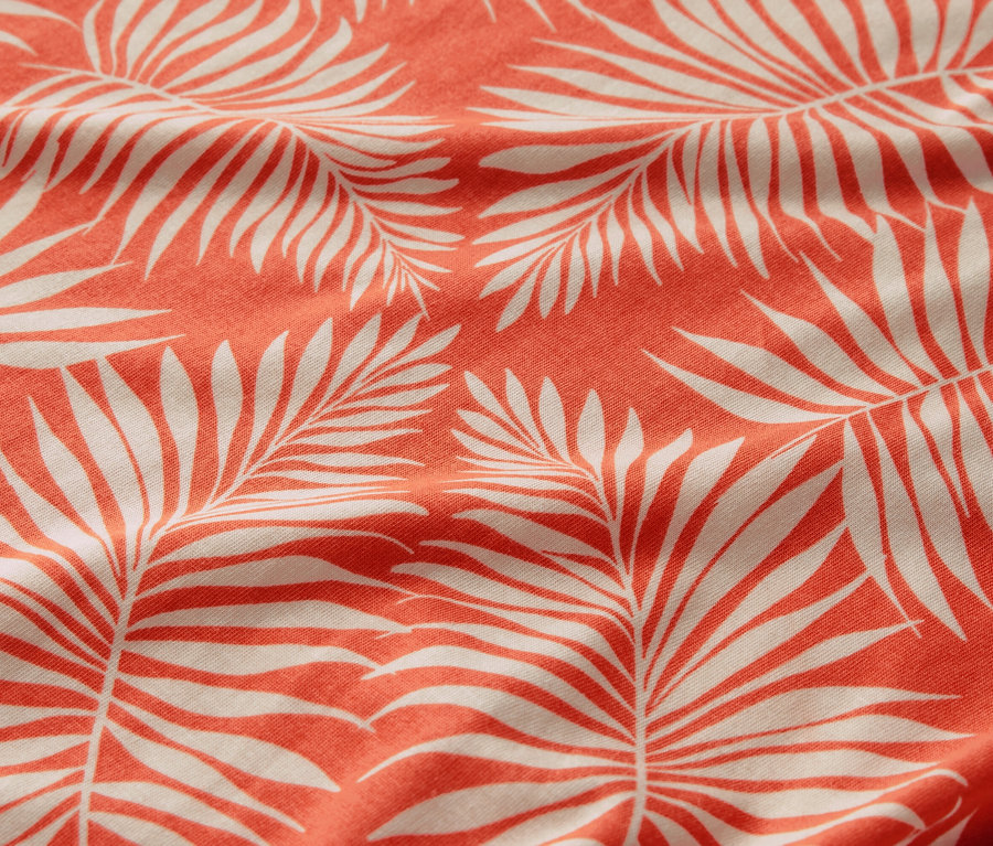 Mercan rengi arka plan üzerinde beyaz palmiye yaprağı desenli, baskılı bir bluz gömleğinin yakın çekimi.
