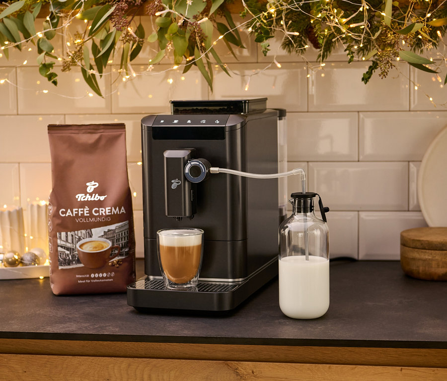 Bir fincan kahve ve bir paket kahve kreması ile birlikte »Esperto 2 Milk« Granite Black kahve makinesi. Süt, cam bir kapta saklanır.