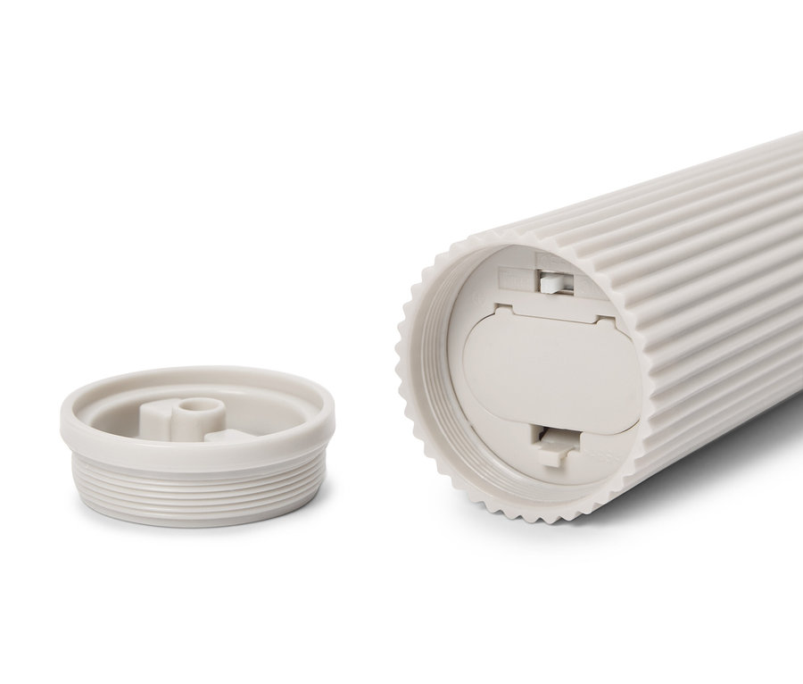 Krem rengi, oluklu, silindir şeklinde bir kap yan yatıyor, kapağı yanında duruyor.