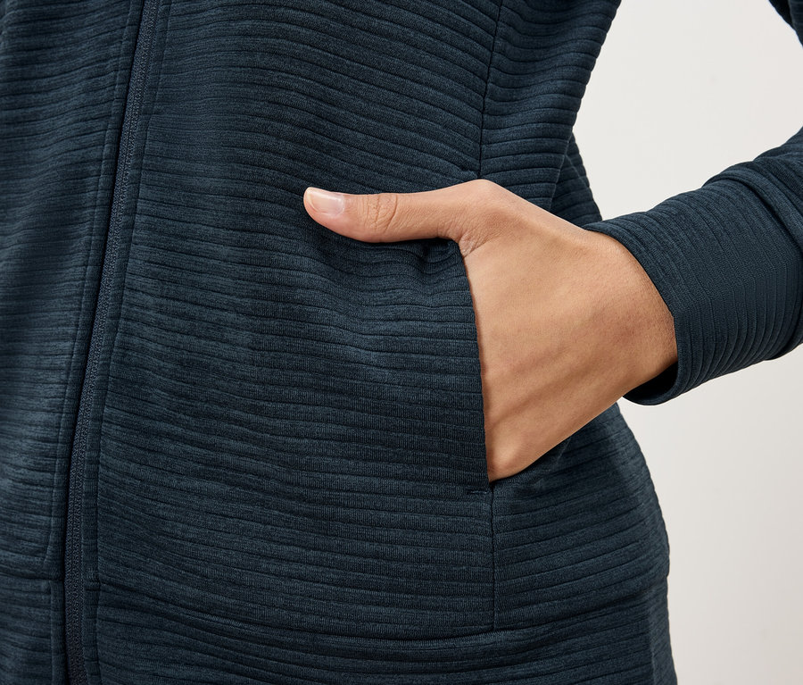 Koyu lacivert dokulu bir ceket giyen ve elini bir cebe sokan bir kişinin yakın çekimi.