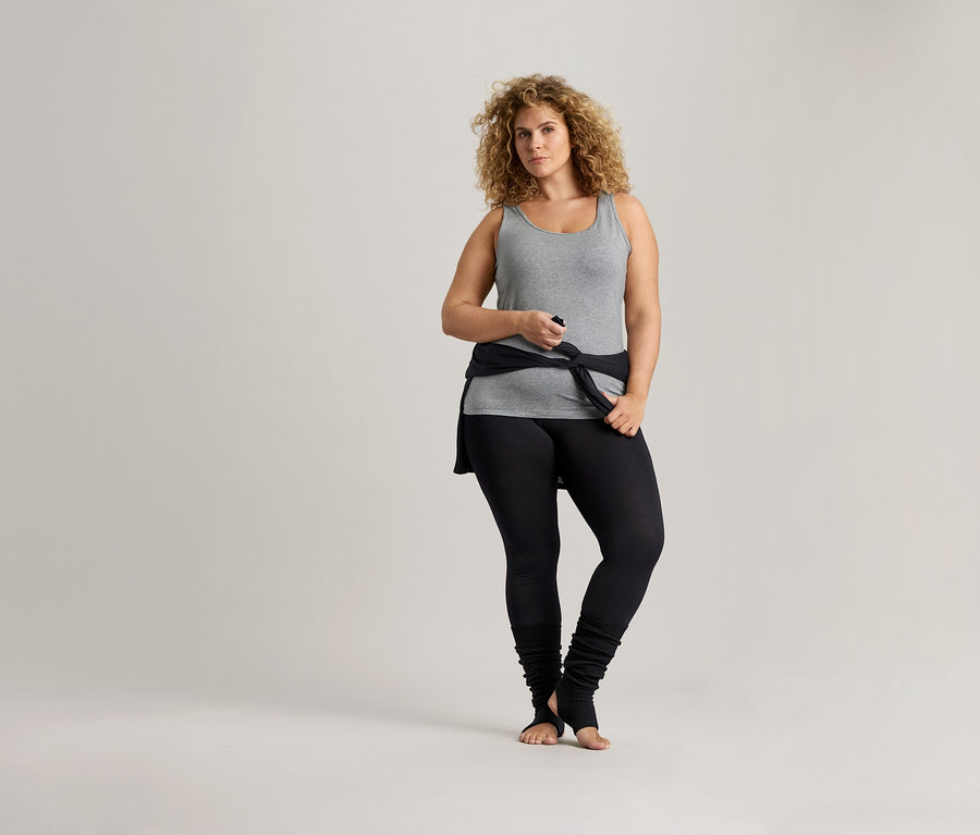 Kıvırcık saçlı kadın gri bir atlet ve siyah tayt giyiyor.