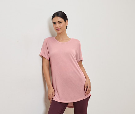 Pembe tişört ve tayt giyen bir kadın beyaz bir duvara yaslanıyor.
