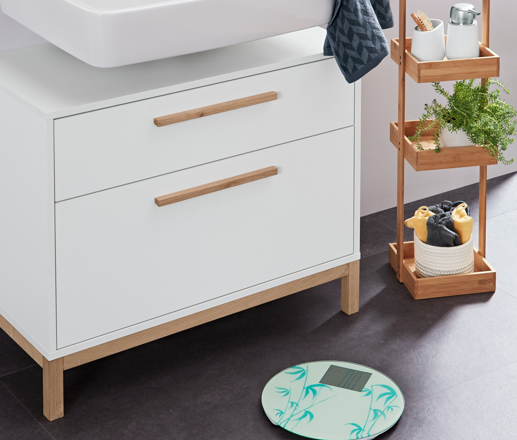 »Eklund« 2 Çekmeceli Lavabo Dolabı üzerinde Beyaz Sıvı Sabunluk ve Saklama Kutusu Seti, yanında Banyo Tartısı ve Antrasit Jakarlı Misafir Havlusu.