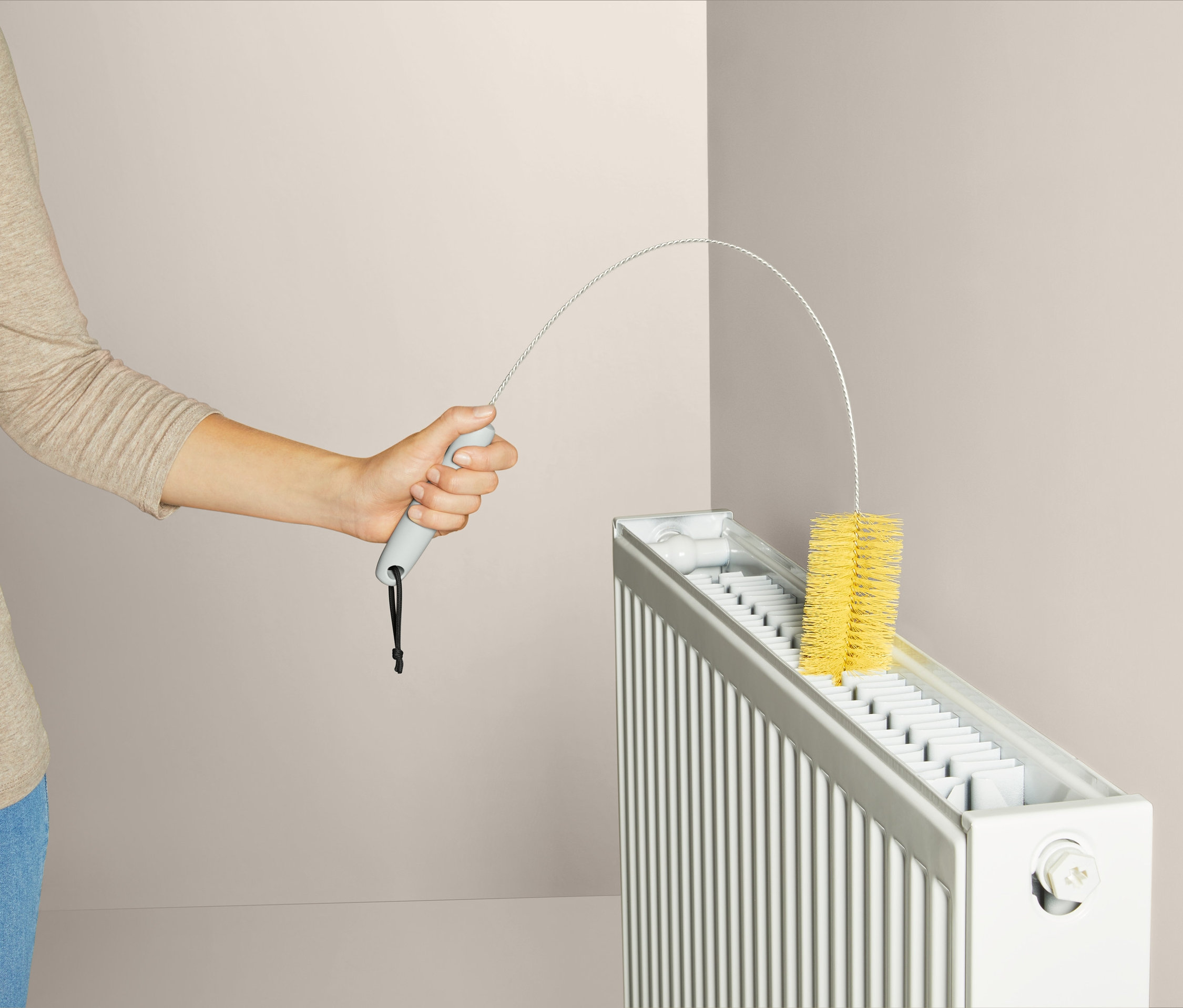 Kadın sarı radyatör fırçasıyla radyatörü temizliyor.