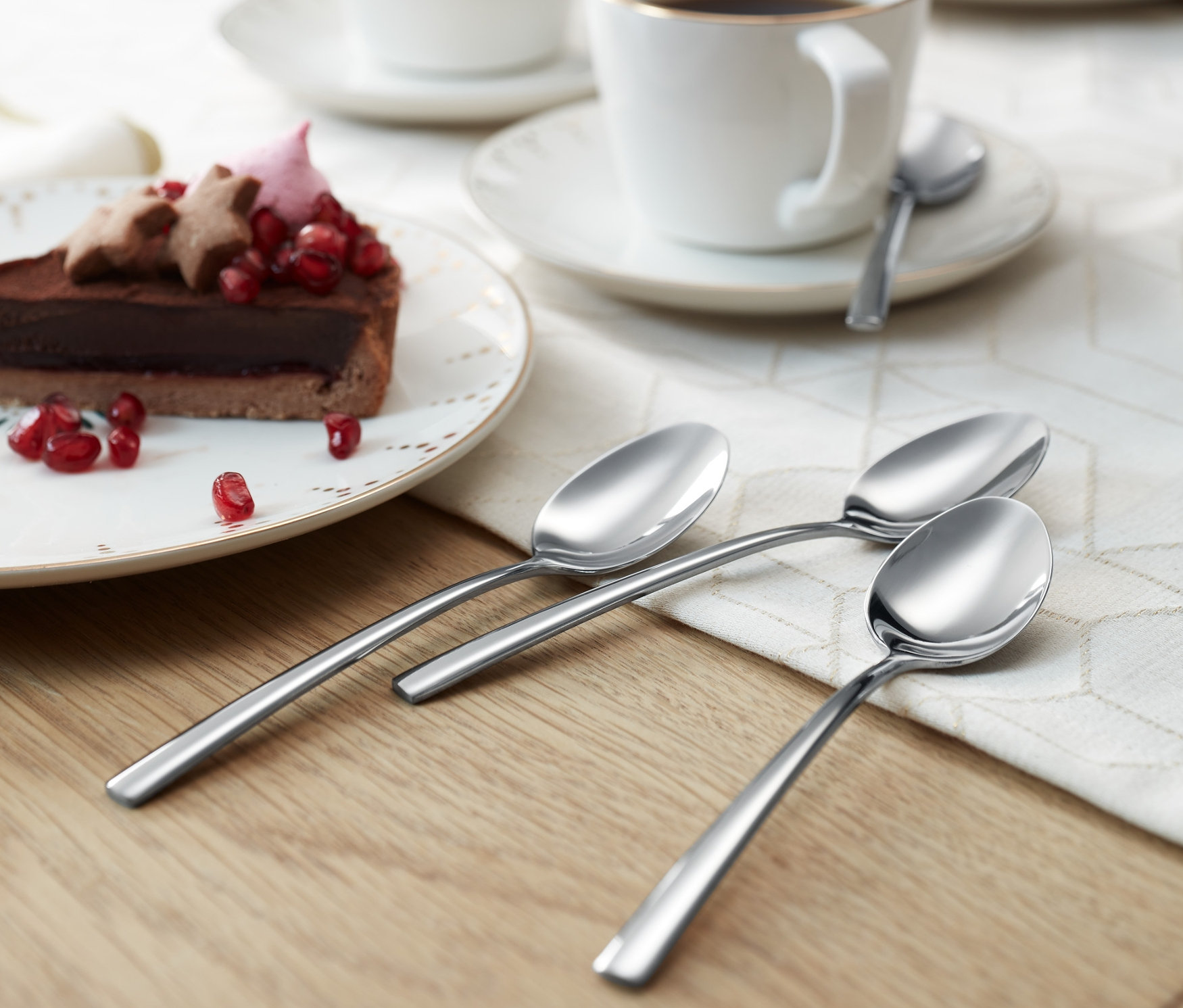 Bir masanın üzerinde çatal bıçak kaşık seti, özellikle 4 adet kahve kaşığı, kahve fincanları ve tatlıların yanında duruyor.