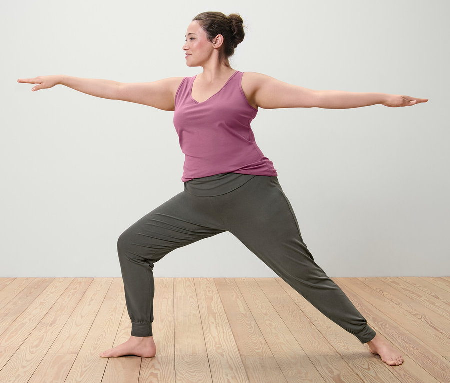 Savaşçı pozisyonunda, eflatun renkli atlet (2'li setten bir adet) ve yoga pantolonu giyen kadın.