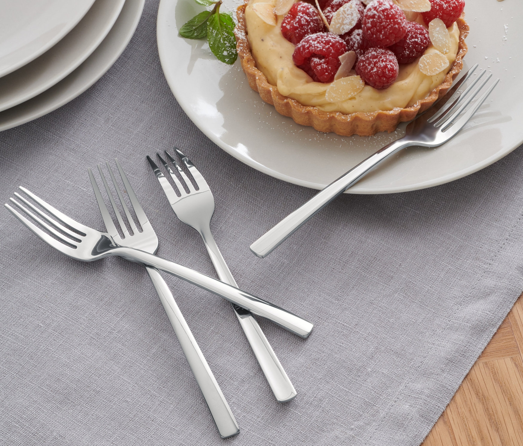 4 Adet Pasta Çatalı'ndan üçü, ahududulu turtanın yanında gri bir masa örtüsü üzerinde duruyor.