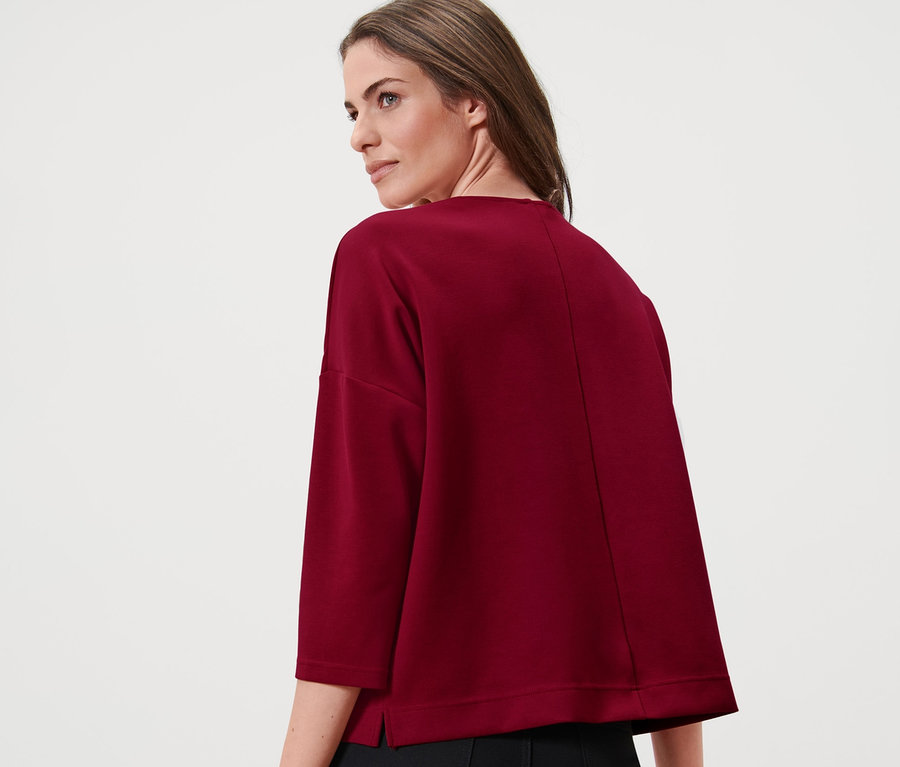 Kadın bordo renkli, 3/4 kollu bir sweatshirt ve siyah pantolon giyiyor.