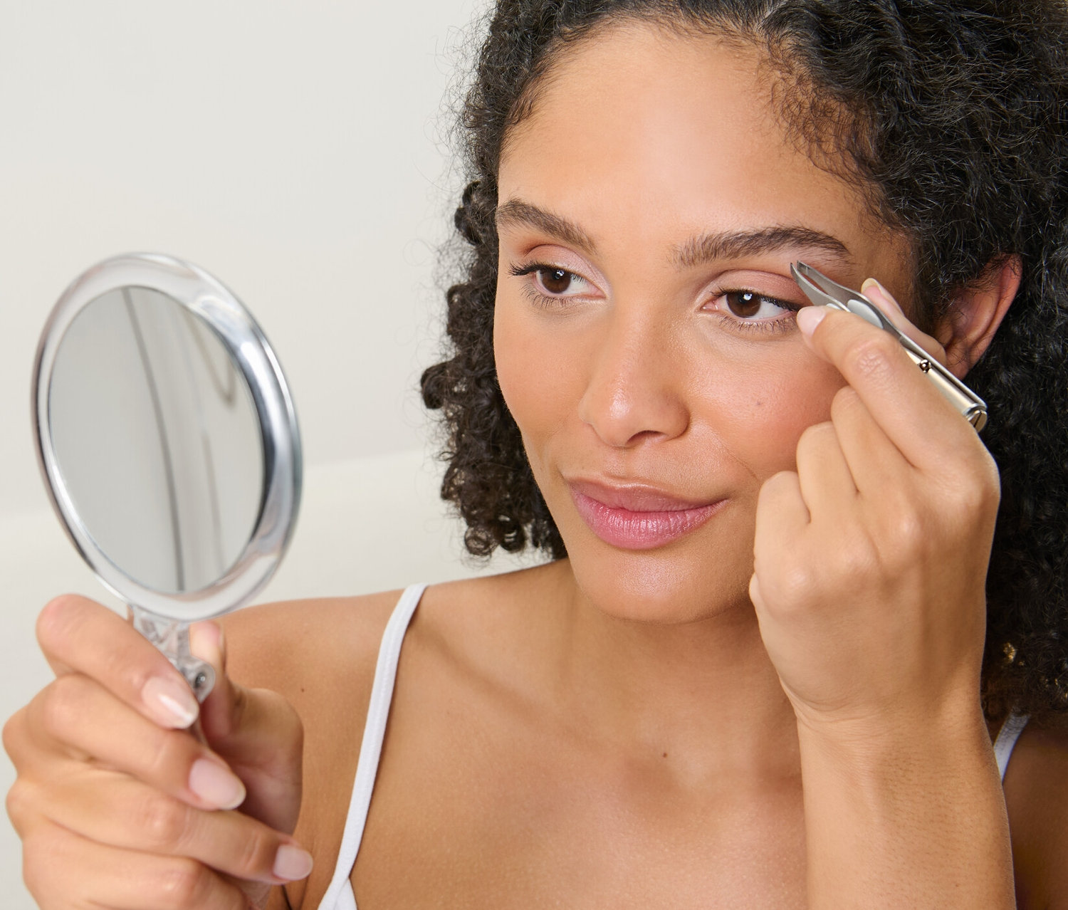 Kadın LED Işıklı Cımbız ile kaşlarını alırken aynaya bakıyor.