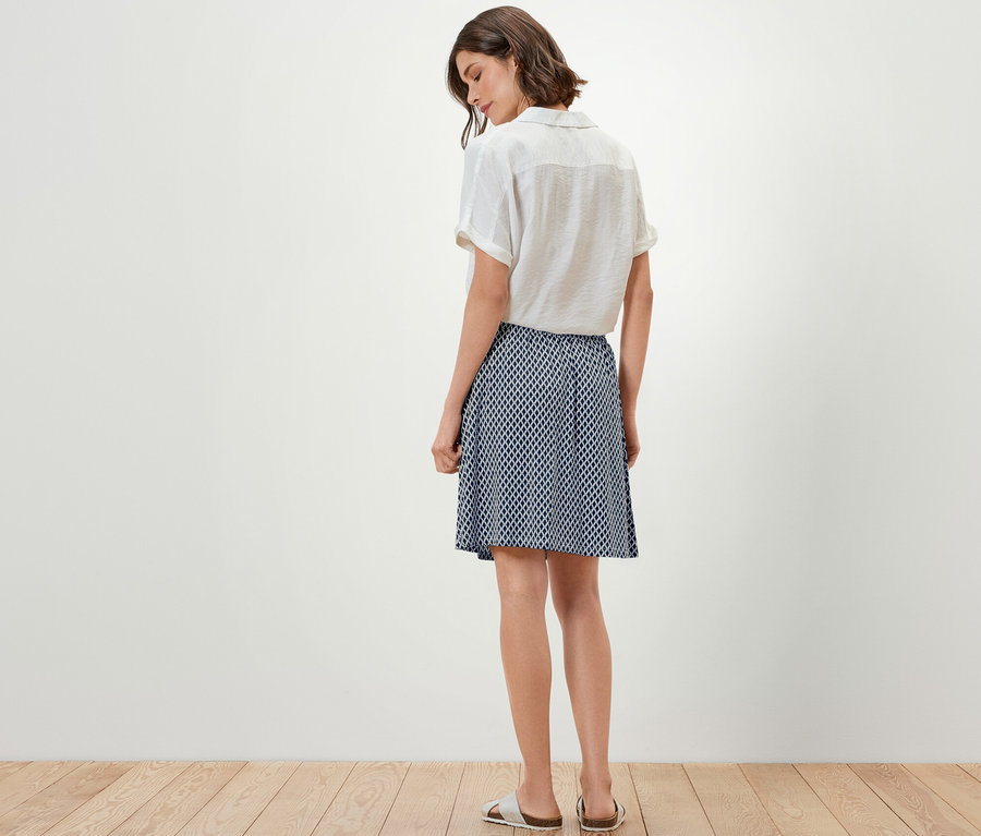 Kadın kameraya arkası dönük duruyor, üzerinde bir üst ve baskılı jarse etek var.