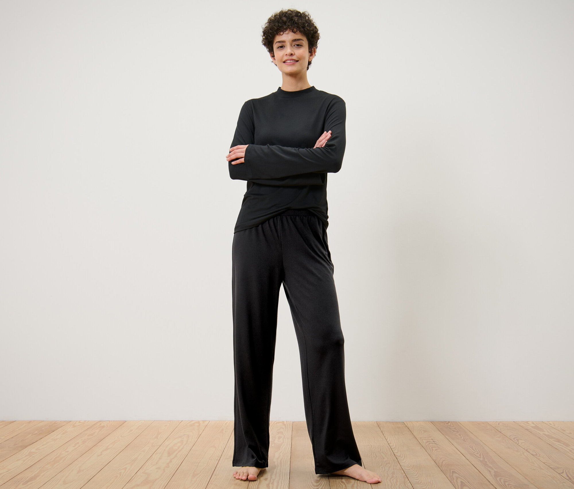 Kadın kolları çapraz bir şekilde duruyor ve geniş eşofman altı giyiyor.