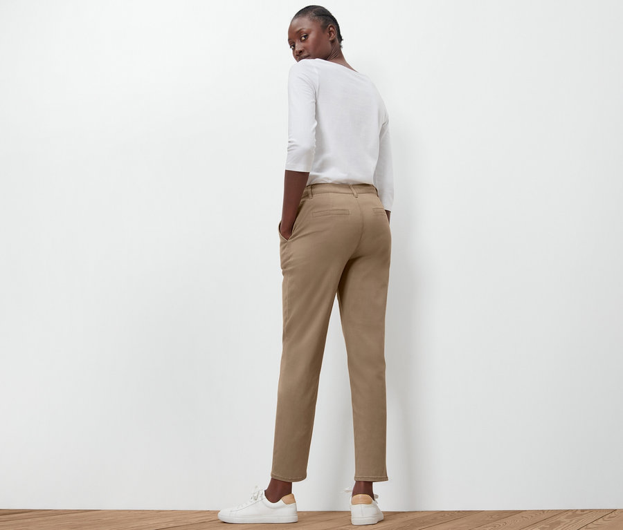 Kadın kameraya arkası dönük bej rengi chino pantolonla poz veriyor.