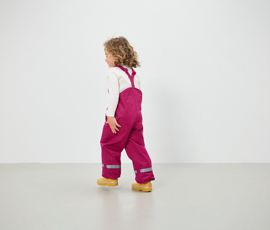 Pembe salopet ve sarı ayakkabılı kız yerde yürüyor.