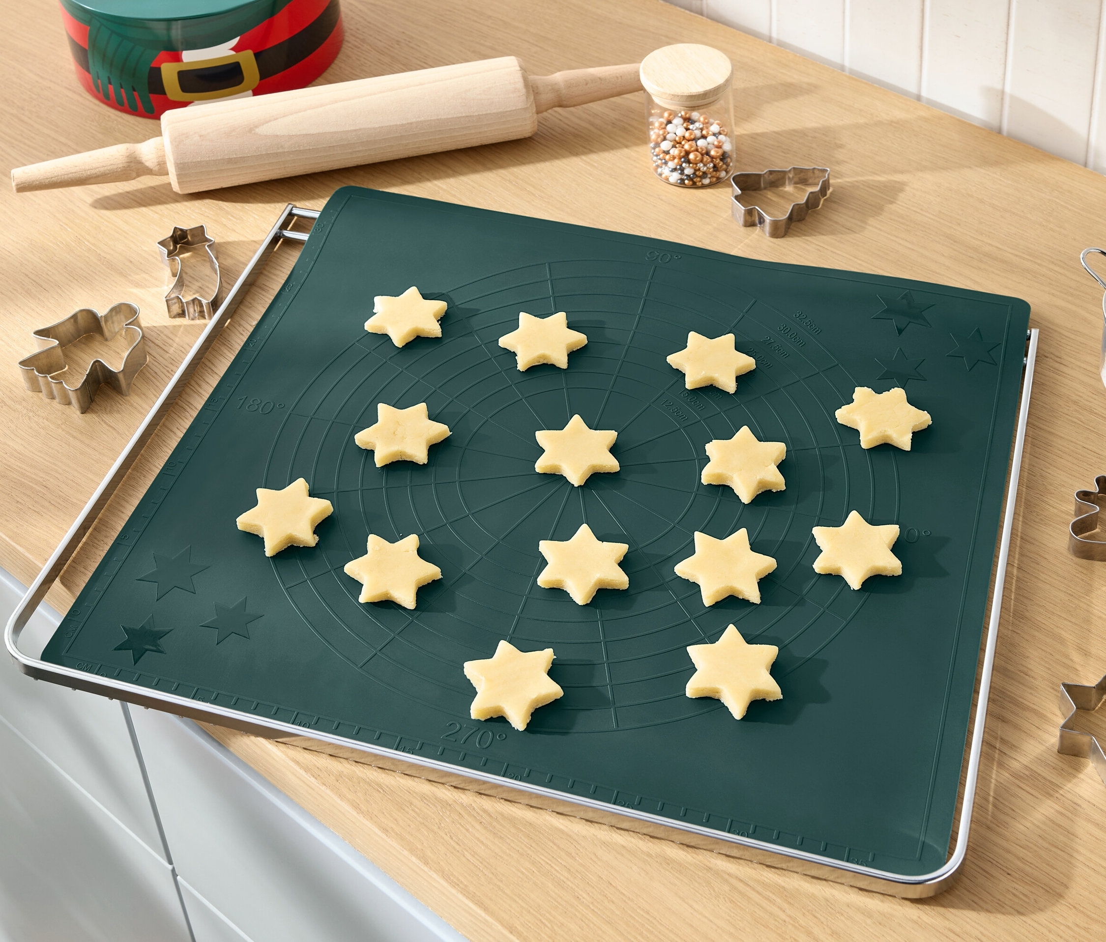 Oklava, şekerlemeler ve kurabiye kalıplarıyla birlikte yeşil bir fırın matı üzerinde hamur yıldızları. 