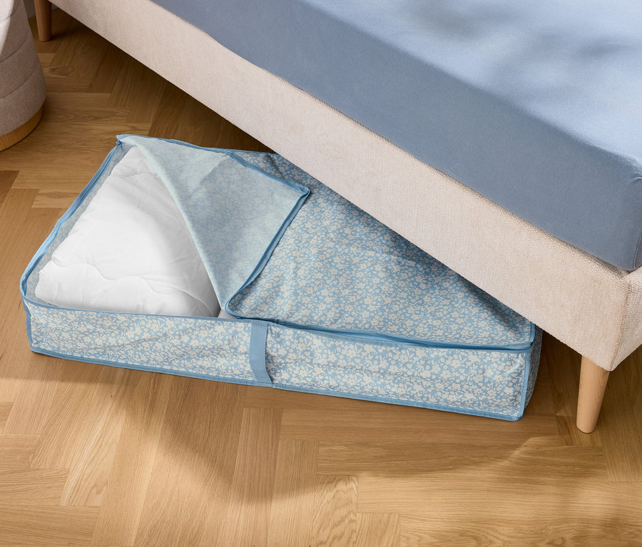 Bir yatağın altında beyaz dolgulu mavi bir saklama çantası duruyor.