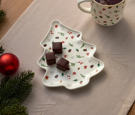 Noel ağacı şeklinde tabakta üç çikolata küpü, yanında bir fincan ve Noel süsü.