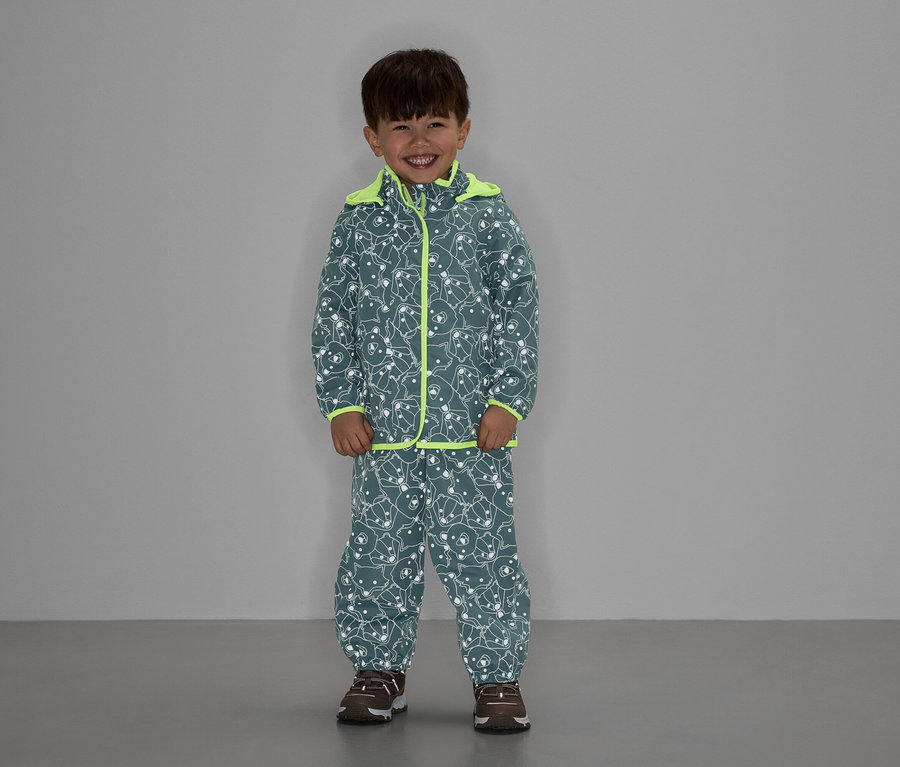 Neon sarısı detaylı, gri ayı desenli ceket ve pantolon giyen bir çocuk gülümsüyor.