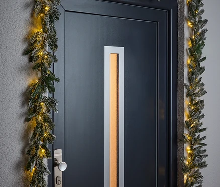Küçük ışıklarla bir Noel çelengiyle çerçevelenmiş siyah bir kapı.