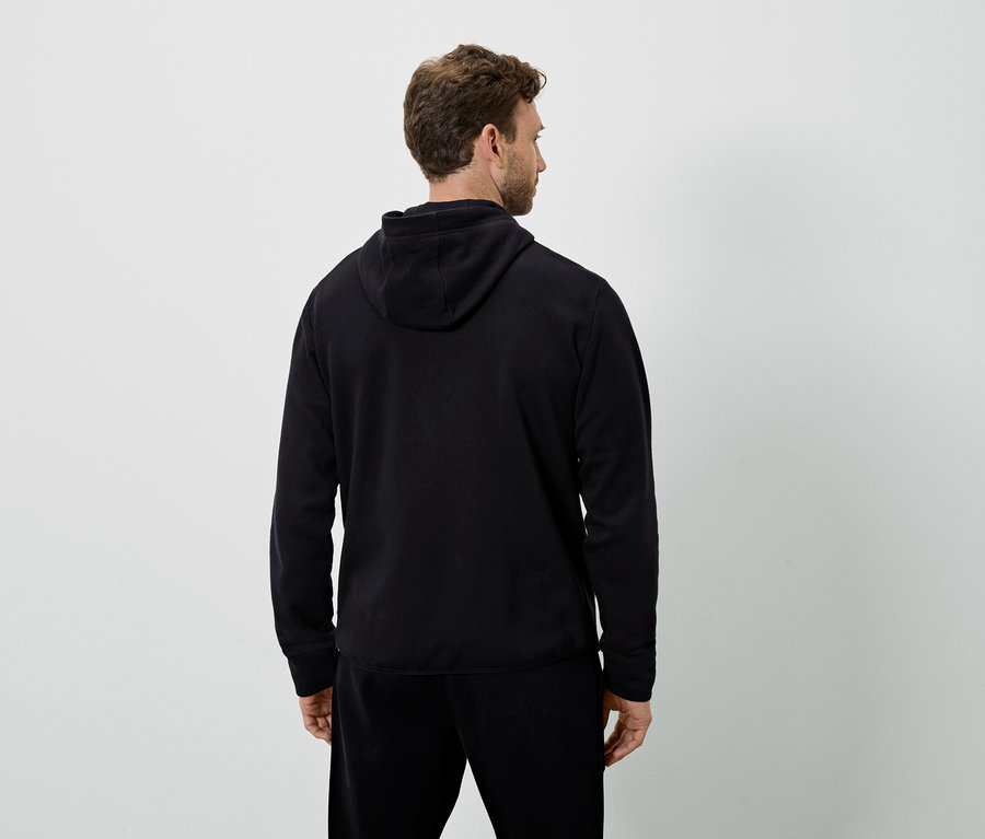 Arkası dönük bir adam siyah kapüşonlu sweatshirt ve siyah eşofman altı giyiyor.