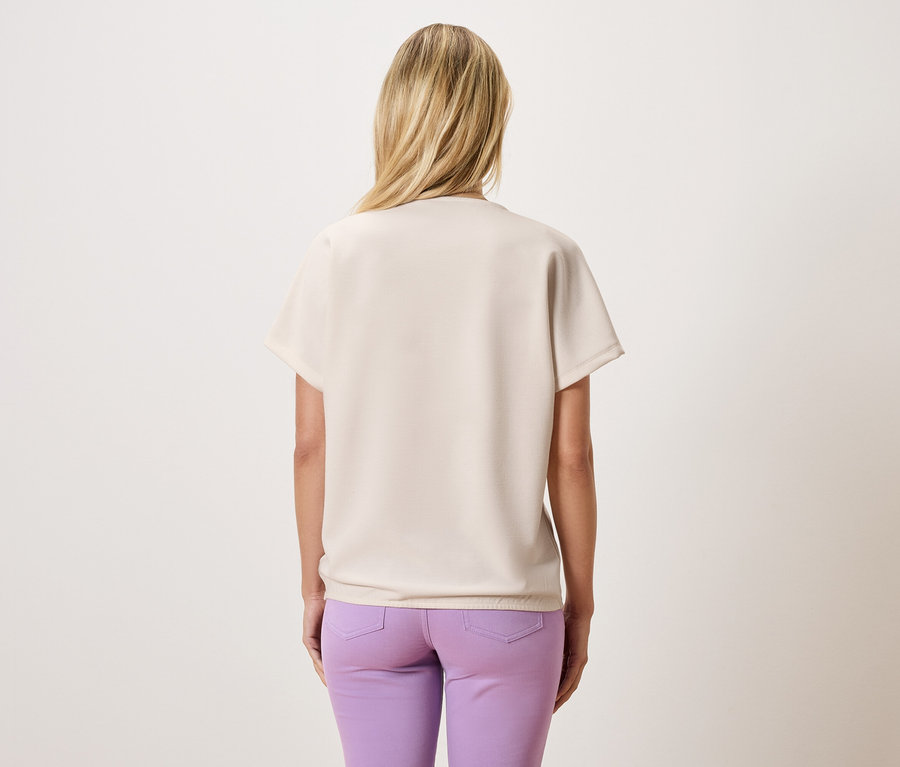 Sarışın saçlı, bej rengi bir bluz ve mor pantolon giyen bir kadının arka görüntüsü.