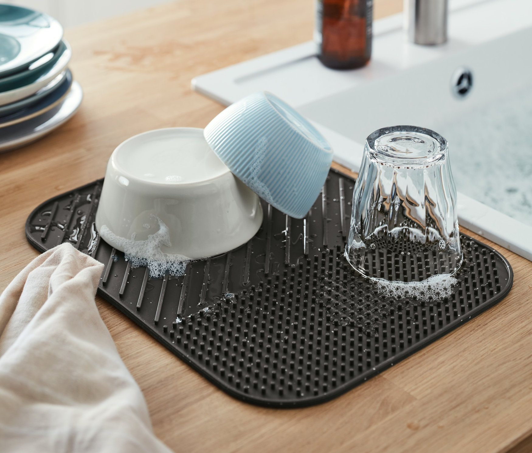 Lavabonun yanında bulaşıklarla birlikte duran gri bir silikon kurutma matı.