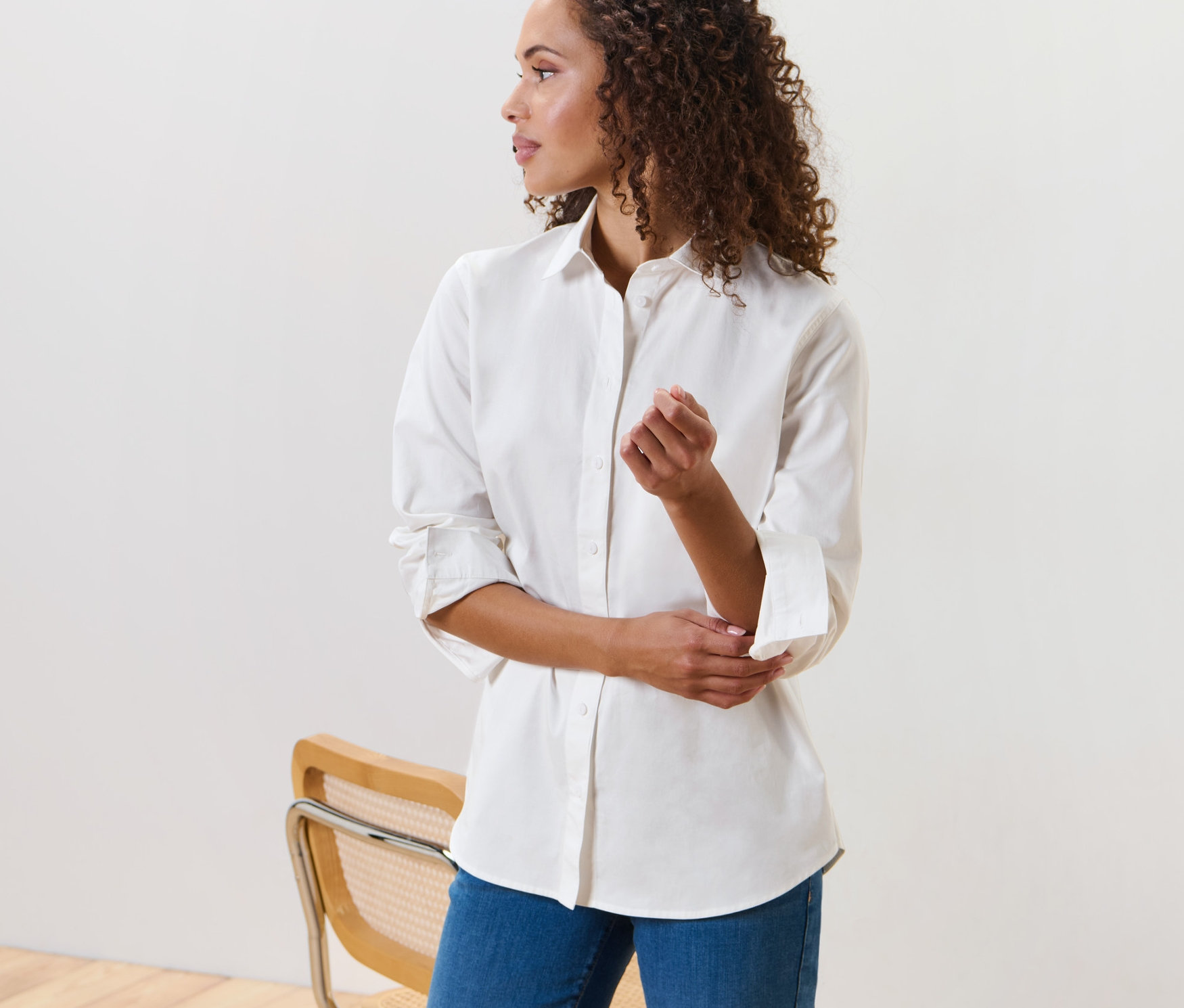 Kahverengi kıvırcık saçlı bir kadın, beyaz bluz ile poz veriyor.