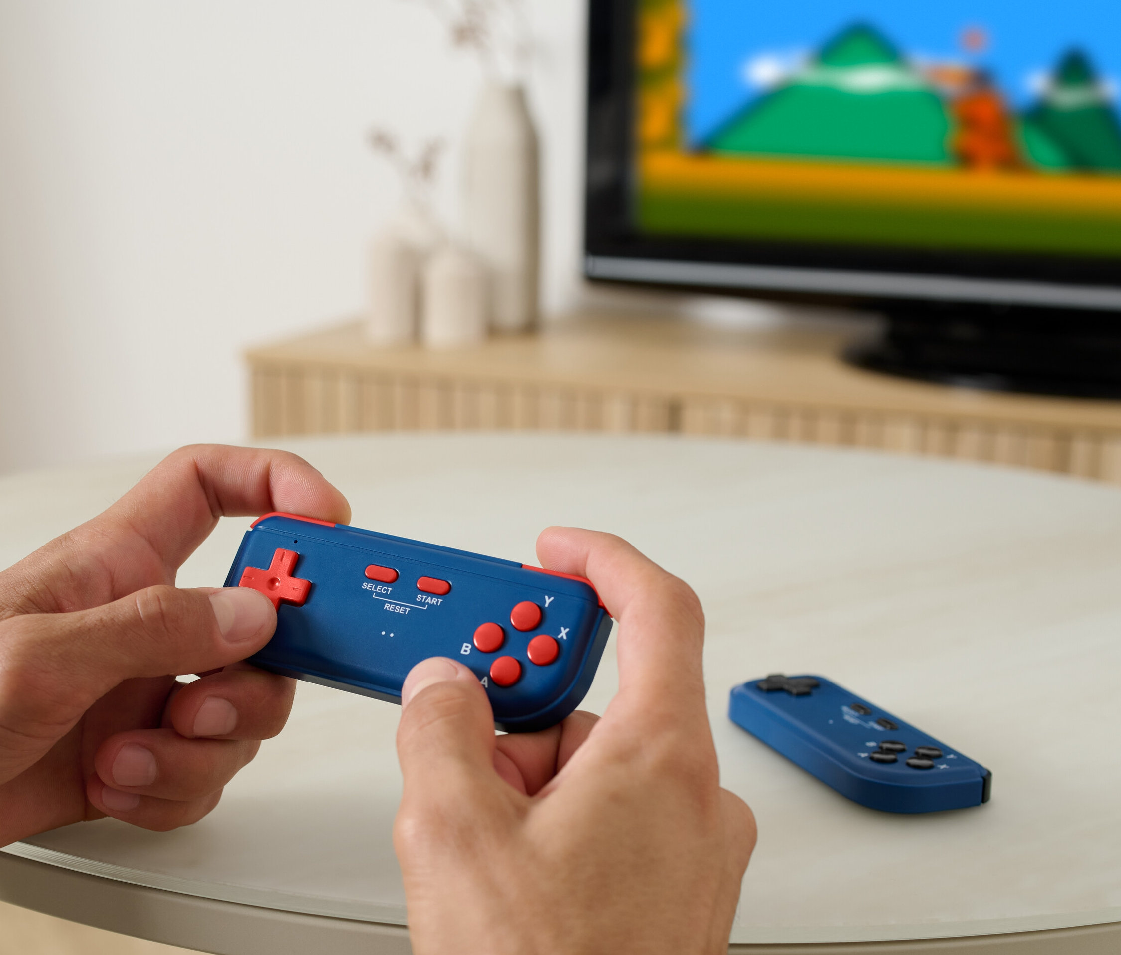 Adam Retro TV Oyun Konsolu oynuyor, arka planda bir televizyon var.