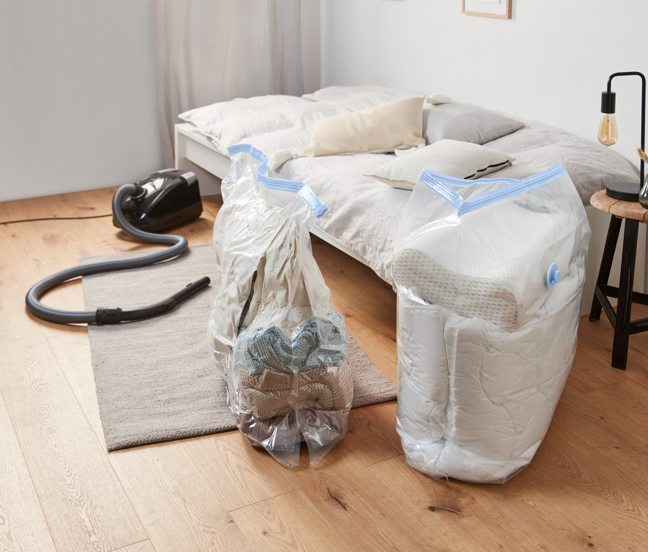 İki adet Vakumlu hurç, küp, yerde bir elektrikli süpürgenin yanında duruyor.