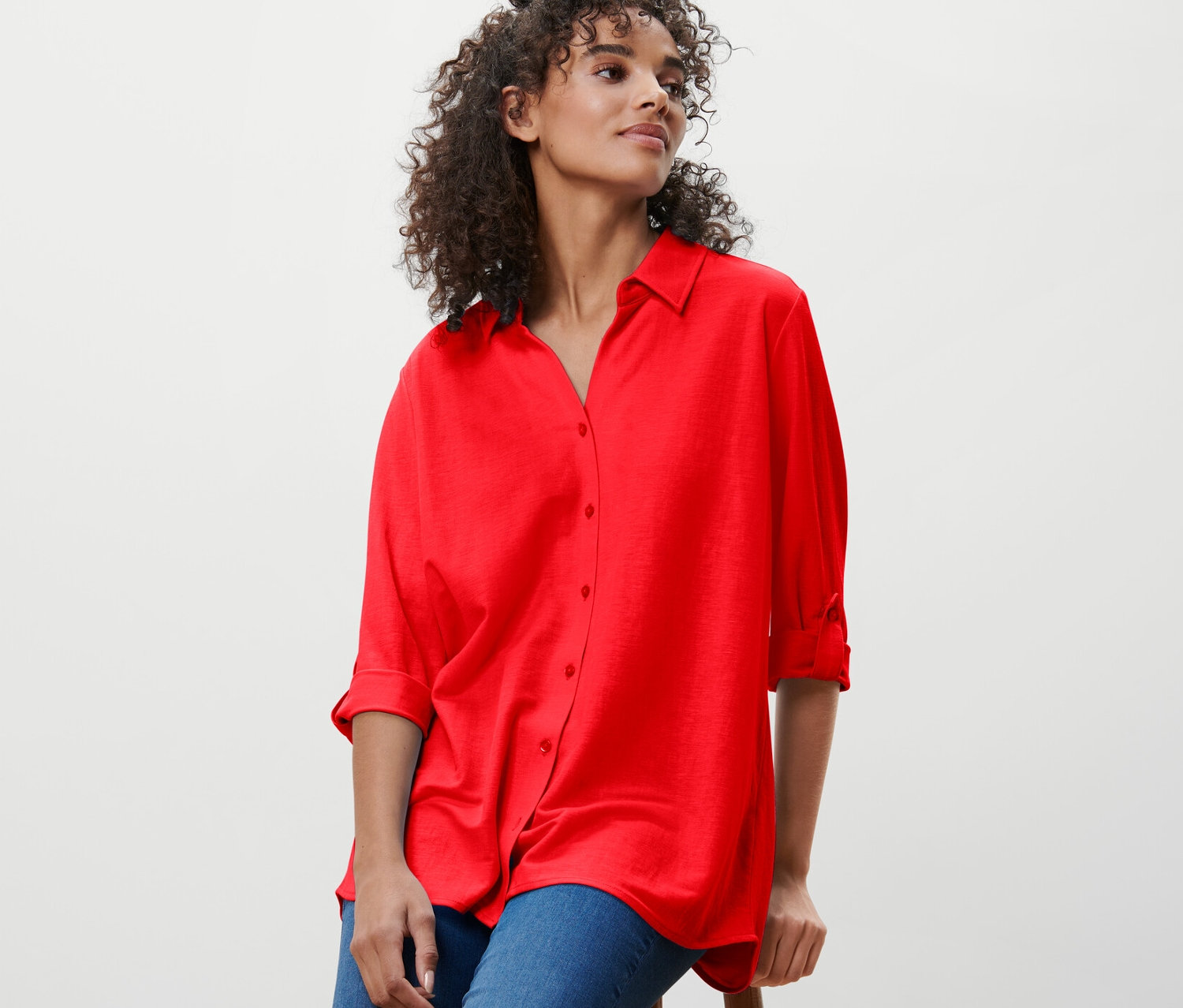 Kadın bir taburede oturuyor ve kırmızı Pike Jersey Bluz giyiyor.