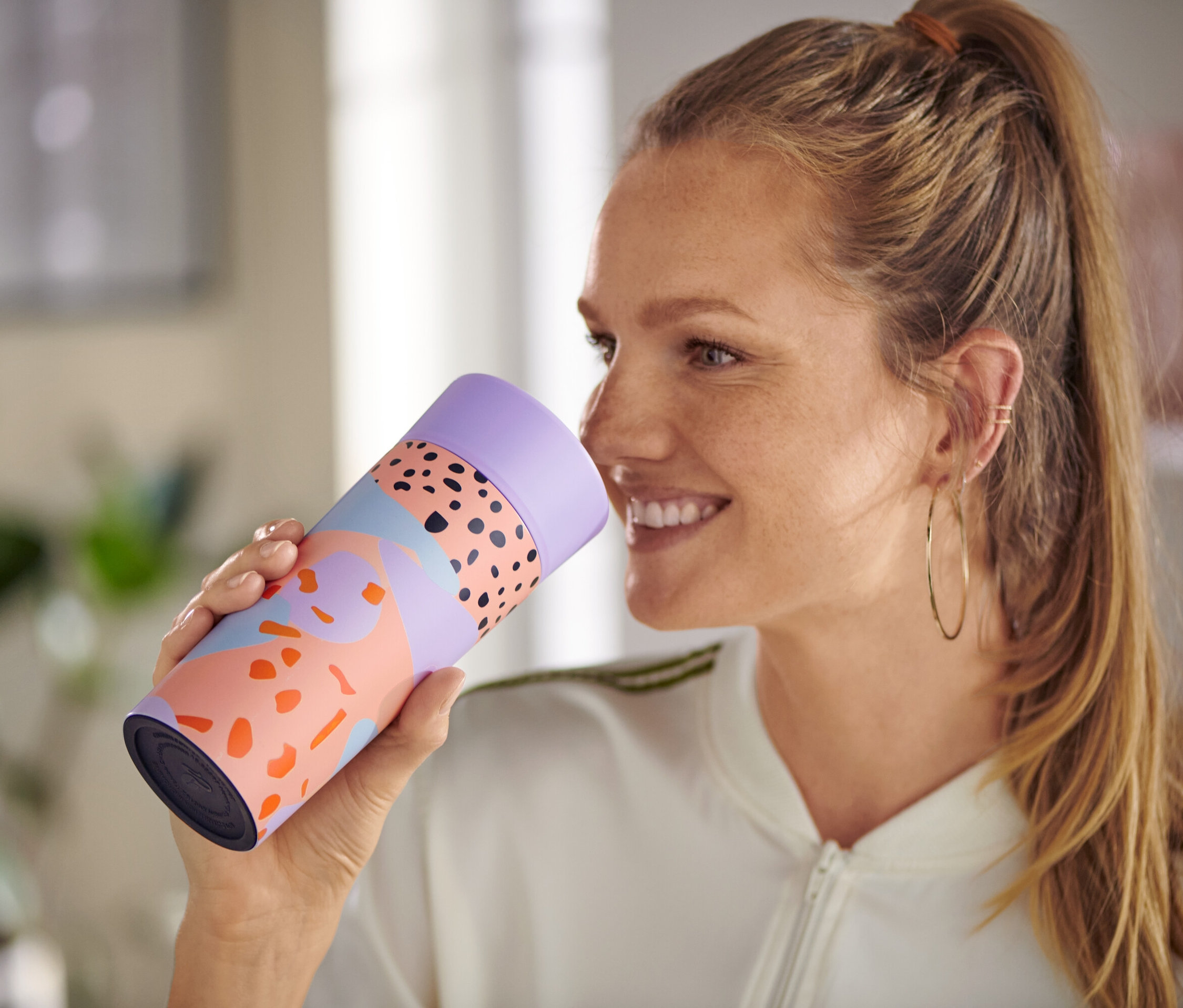 Gülümseyen bir kadın, hibrit kayısı rengi Al-Götür Kahve Bardağı tutuyor.