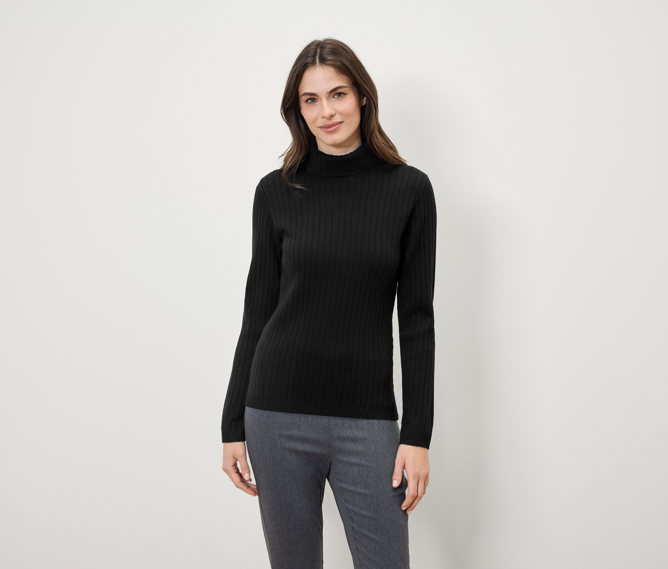 Kadın siyah balıkçı yaka kazak ve gri pantolon giyiyor.