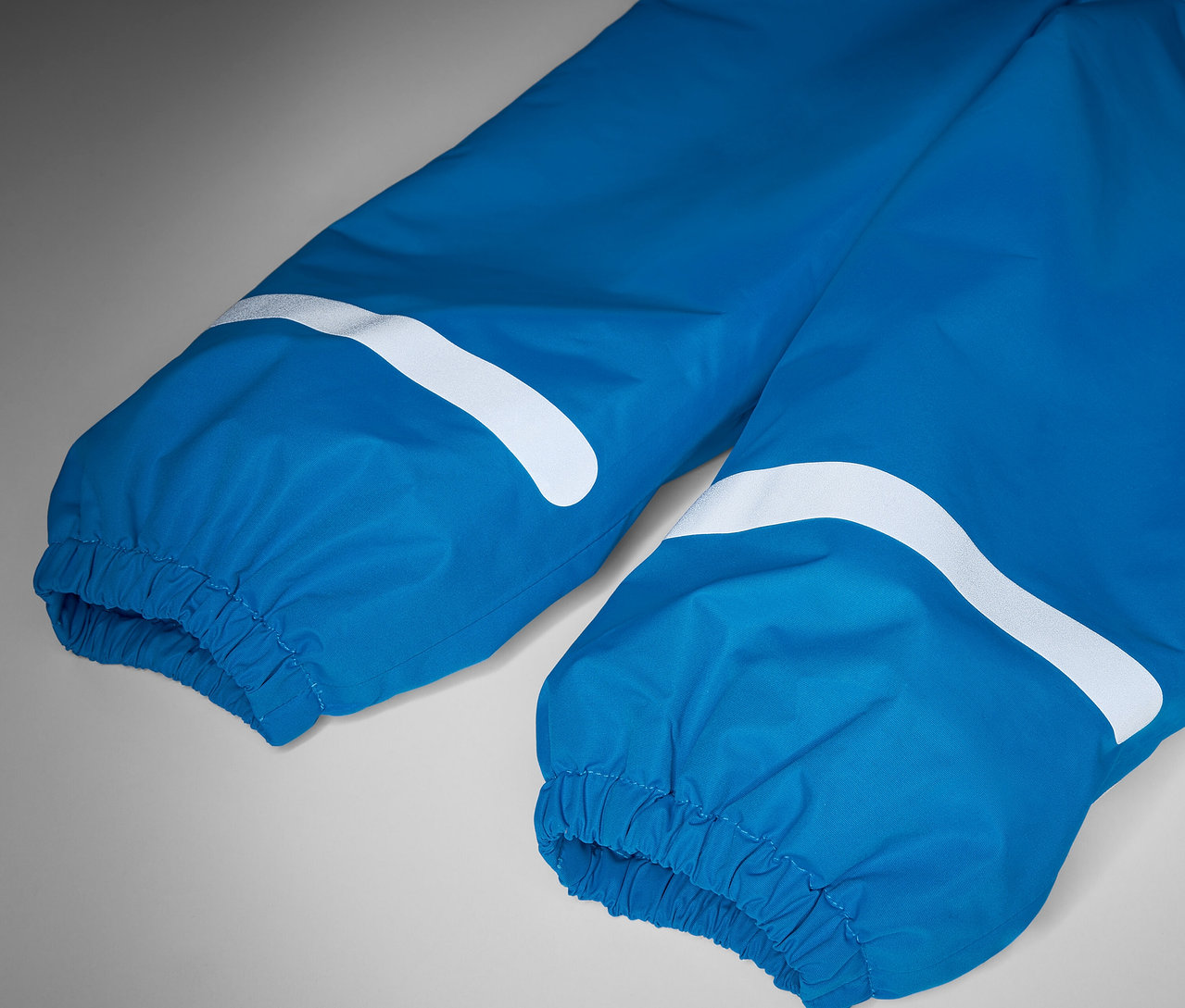 Beyaz reflektörlü şeritlere sahip mavi çocuk termal yağmur pantolonunun detayı.