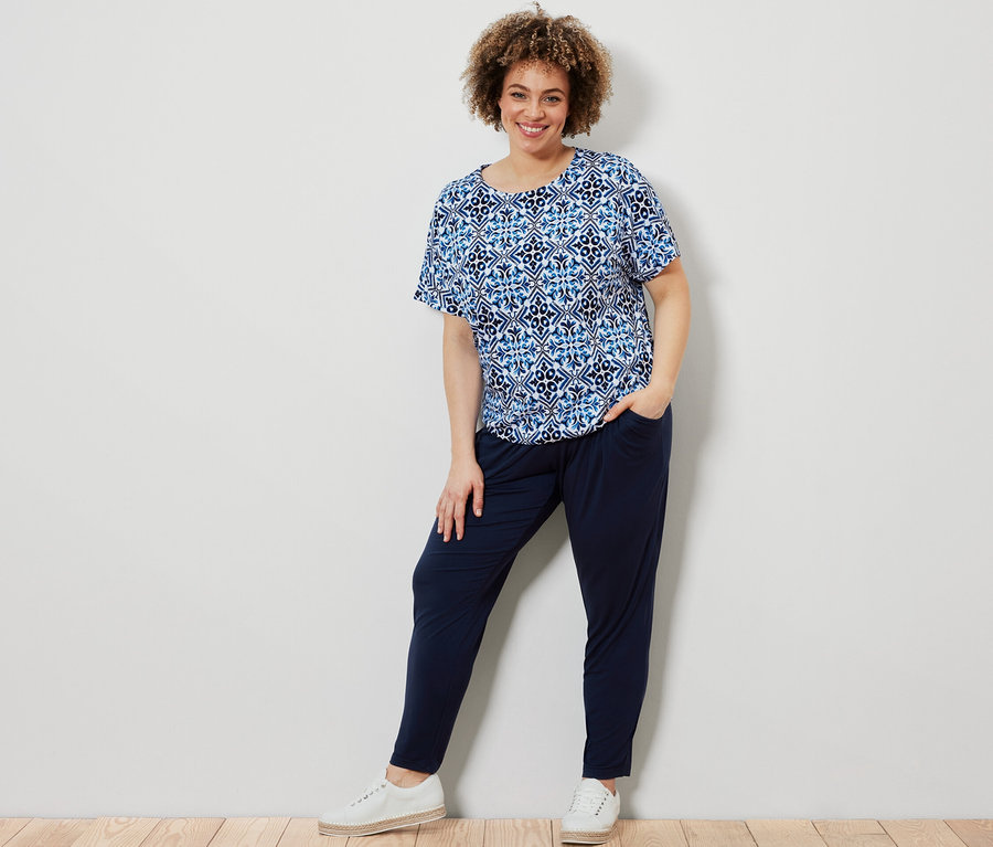 Kadın mavi, baskılı bluz ve lacivert jarse pantolonla poz veriyor.