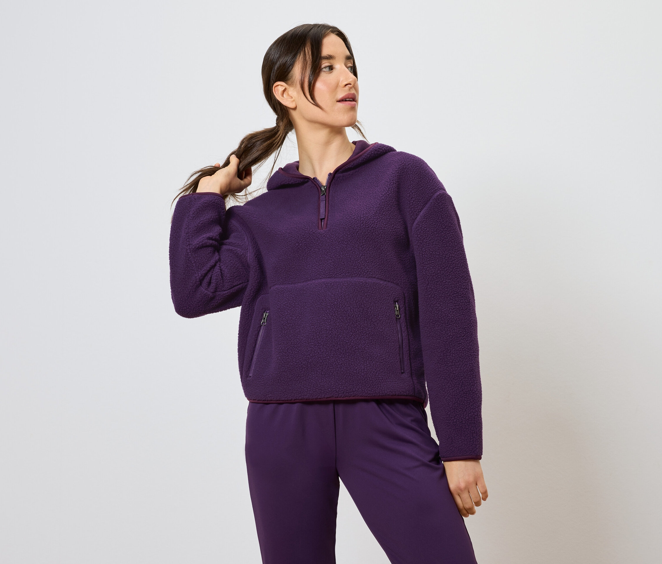 Kadın at kuyruğu tutuyor, mor kapüşonlu sweatshirt ve pantolon giyiyor.