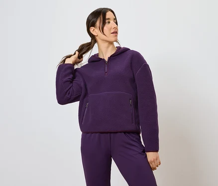 Kadın at kuyruğu tutuyor, mor kapüşonlu sweatshirt ve pantolon giyiyor.
