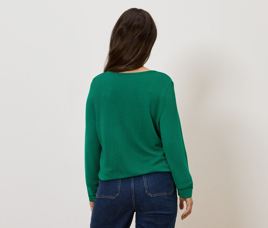 Kadın arkası dönük, yeşil bir kazak ve kot pantolon giyiyor.