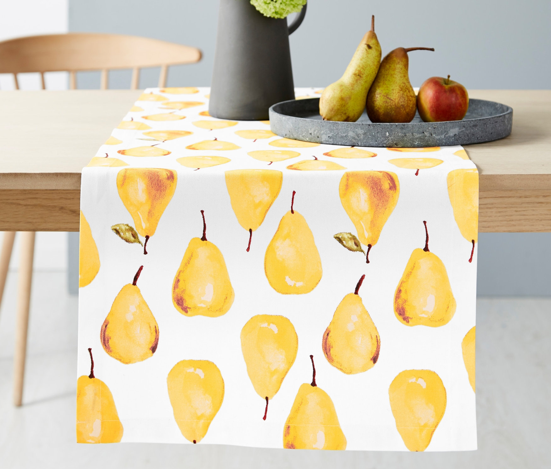 Masanın üzerinde armut desenli Runner Masa Örtüsü, beyaz çiçekli vazo ve meyve tabağı bulunmaktadır.