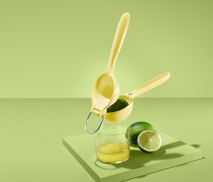 Yeşil arka planda bir bardak meyve suyunun ve bir limonun üzerinde sarı bir narenciye sıkacağı.