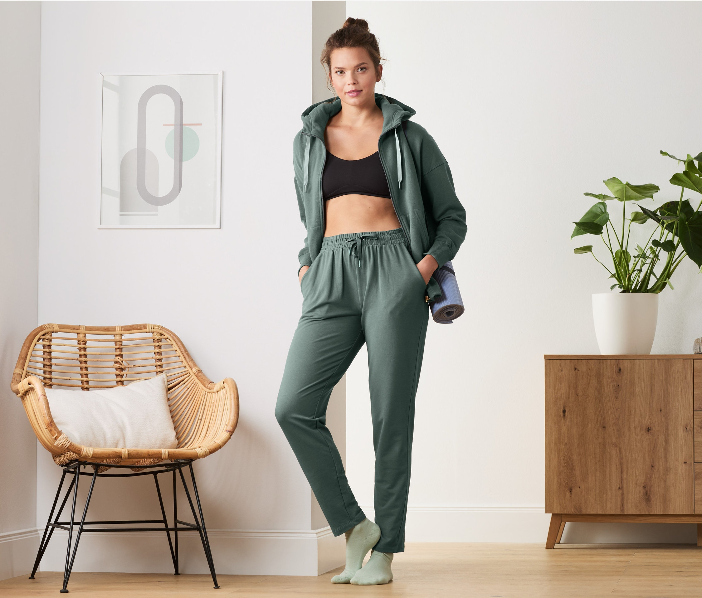 Kadın koyu yeşil eşofman altı ve kapüşonlu ceketle ayakta duruyor.