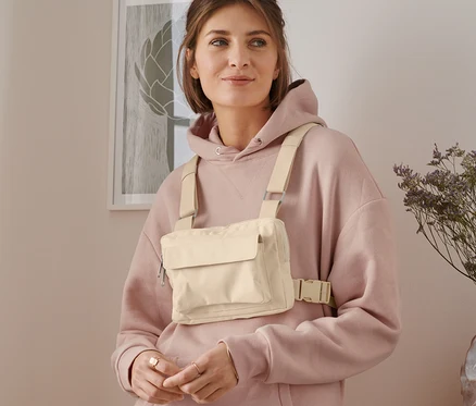 Kadın bej rengi değişken omuz çantası ve pembe kapüşonlu sweatshirt giyiyor.